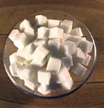 a photo of a glass bowl containing sugar cubes, sitting on a wooden table